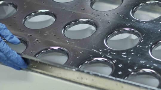 A worker holding a tin plated tray with holes