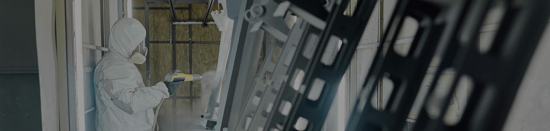 A worker in full suit and mask powder coating a component